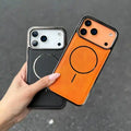 Hand holding two phone cases, one black and one orange with a circular design, on a dark surface.