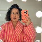 Person wearing a pink and orange striped robe taking a mirror selfie with a phone.