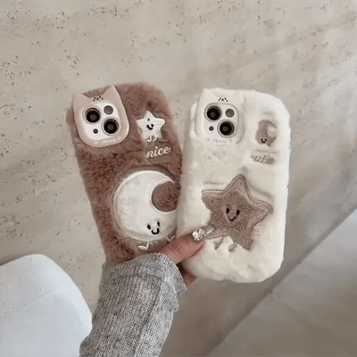 Two fluffy phone cases with cute designs held by a person against a neutral background